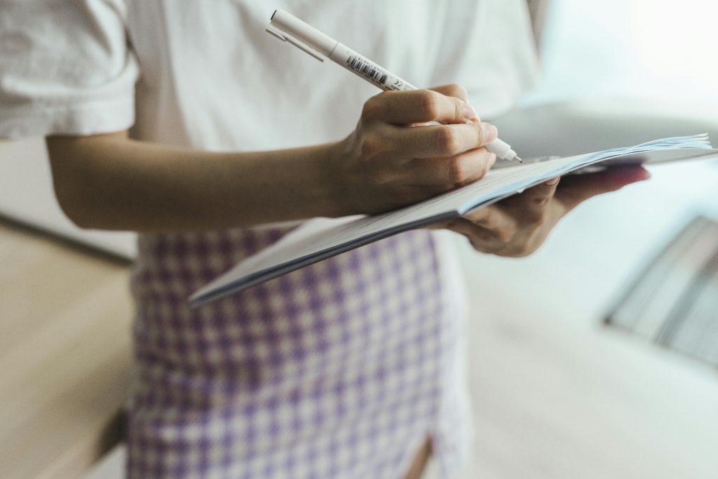 Close-up of an individual writing in a notebook using a pen in an indoor setting.